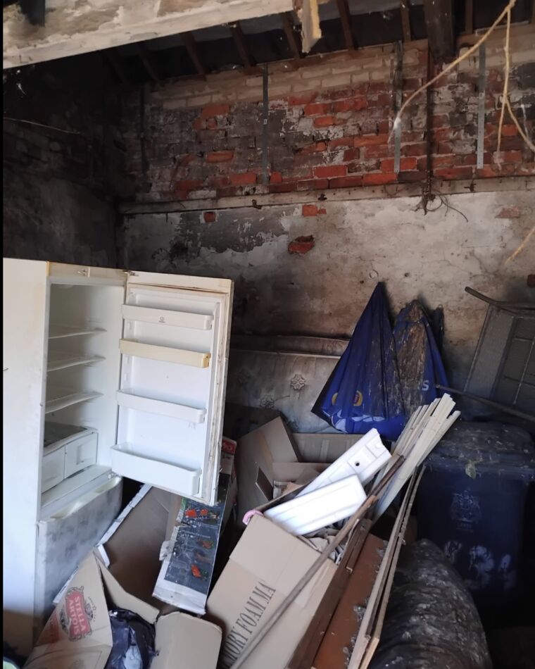 A damp brick outbuilding packed with an old fridge, cardboard and household waste