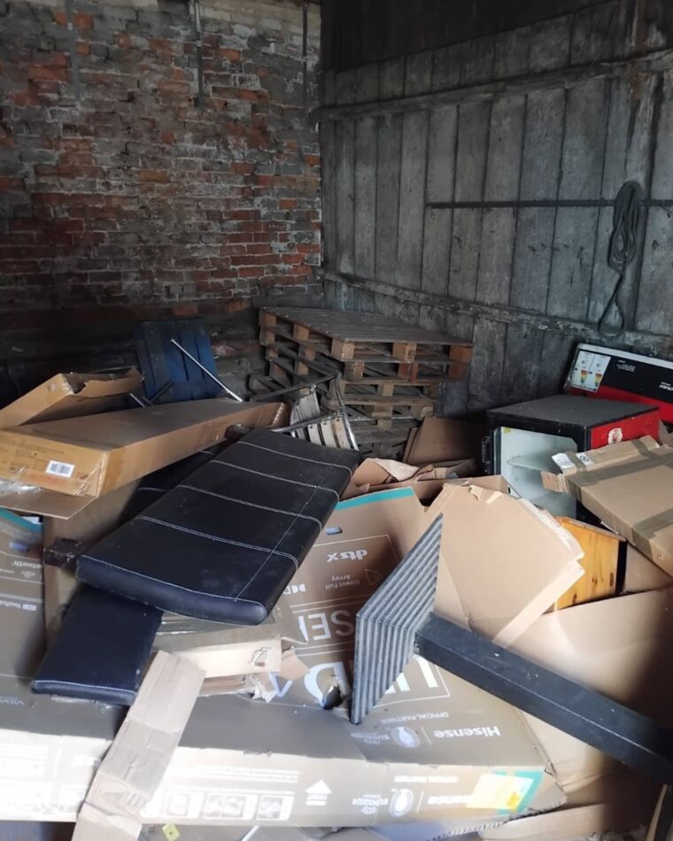 The far corner of the same outbuilding, piled with flat-pack boxes and pallets